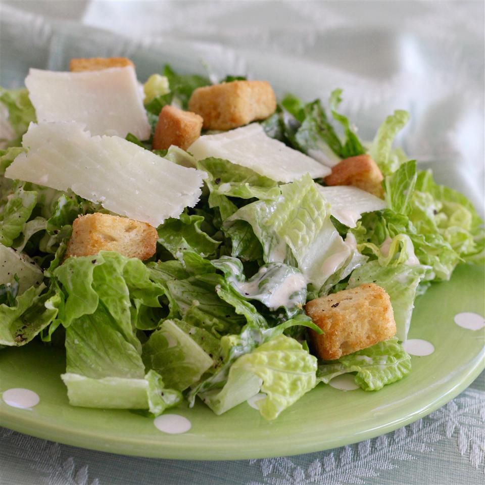 a caesar salad with croutons and shaved Parmesan on a pale green plate
