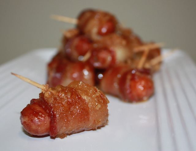 closeup of lil' smokies wrapped in bacon secured with toothpicks, displayed on a white rectangular serving dish
