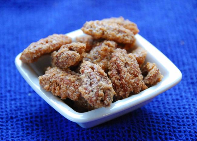 a small square white dish of candied pecan halves on a blue background