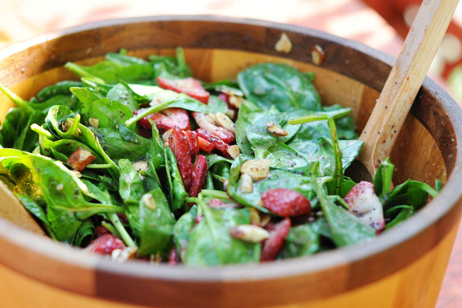A wooden salad bowl with a tossed salad of fresh spinach and strawberries