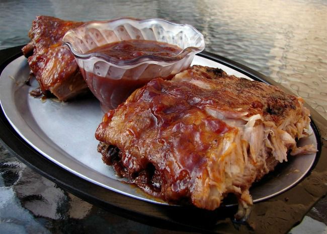 A glass dish of sauce on a platter with baby back ribs