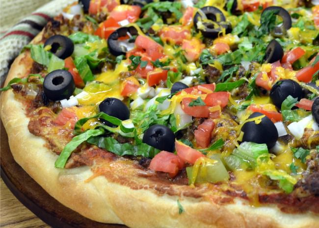 Пицца, посыпанная измельченными листьями салата, маслинами и нарезанными помидорами