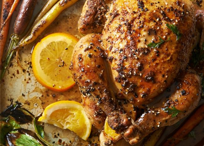 whole chicken in a roasting pan with carrots and orange slices
