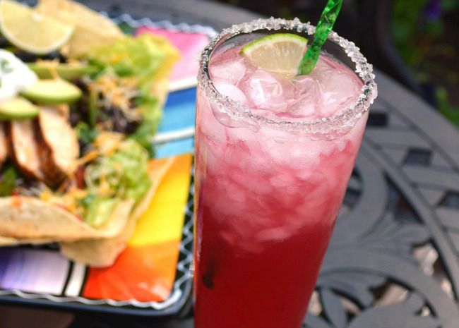 glass with red margarita next to tacos
