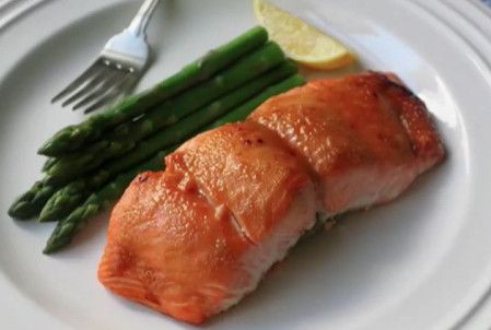 a salmon fillet on a plate with asparagus and a lemon wedge