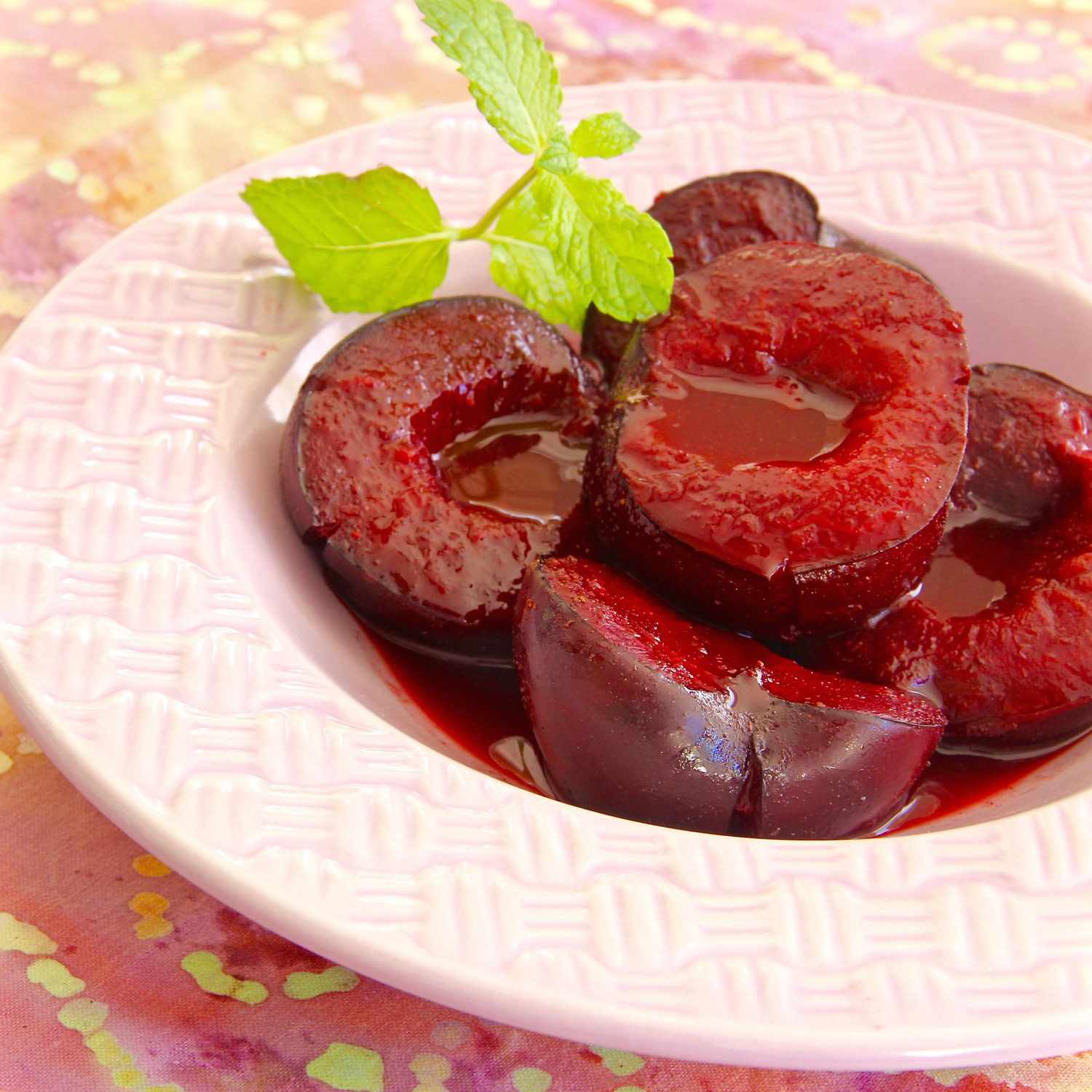 a shallow white bowl with a wide rim filled with juicy-looking red plum halves