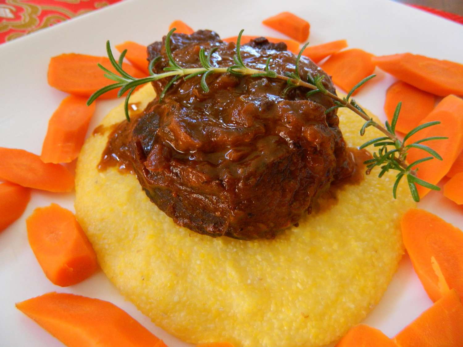 a serving of braised beef ribs on soft polenta, garnished with a fresh thyme sprig