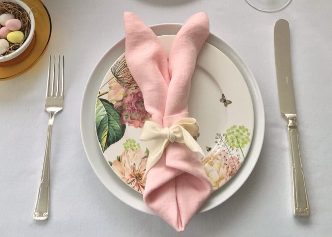 Easter Bunny Ear Napkin tied with a ribbon and lying flat on a decorative plate
