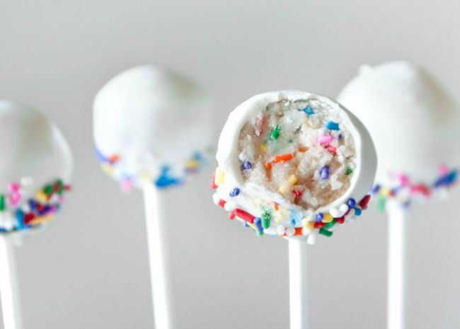 White-coated cake pops on sticks, one with a bite taken out of it so you can see the colored sprinkles inside