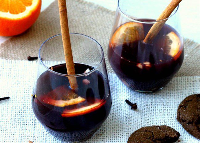 stemless wine glasses with mulled wine garnished with cinnamon sticks, orange slices, and whole cloves