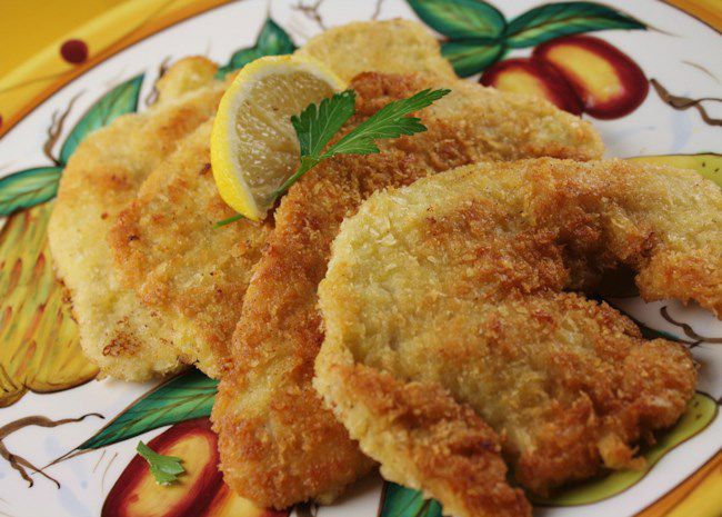 breaded fried cutlets on a colorful painted ceramic plate, garnished with fresh lemon wedges and parsley