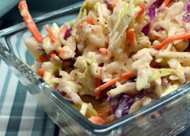 closeup of a square glass dish of coleslaw with shredded carrots and green and purple cabbage
