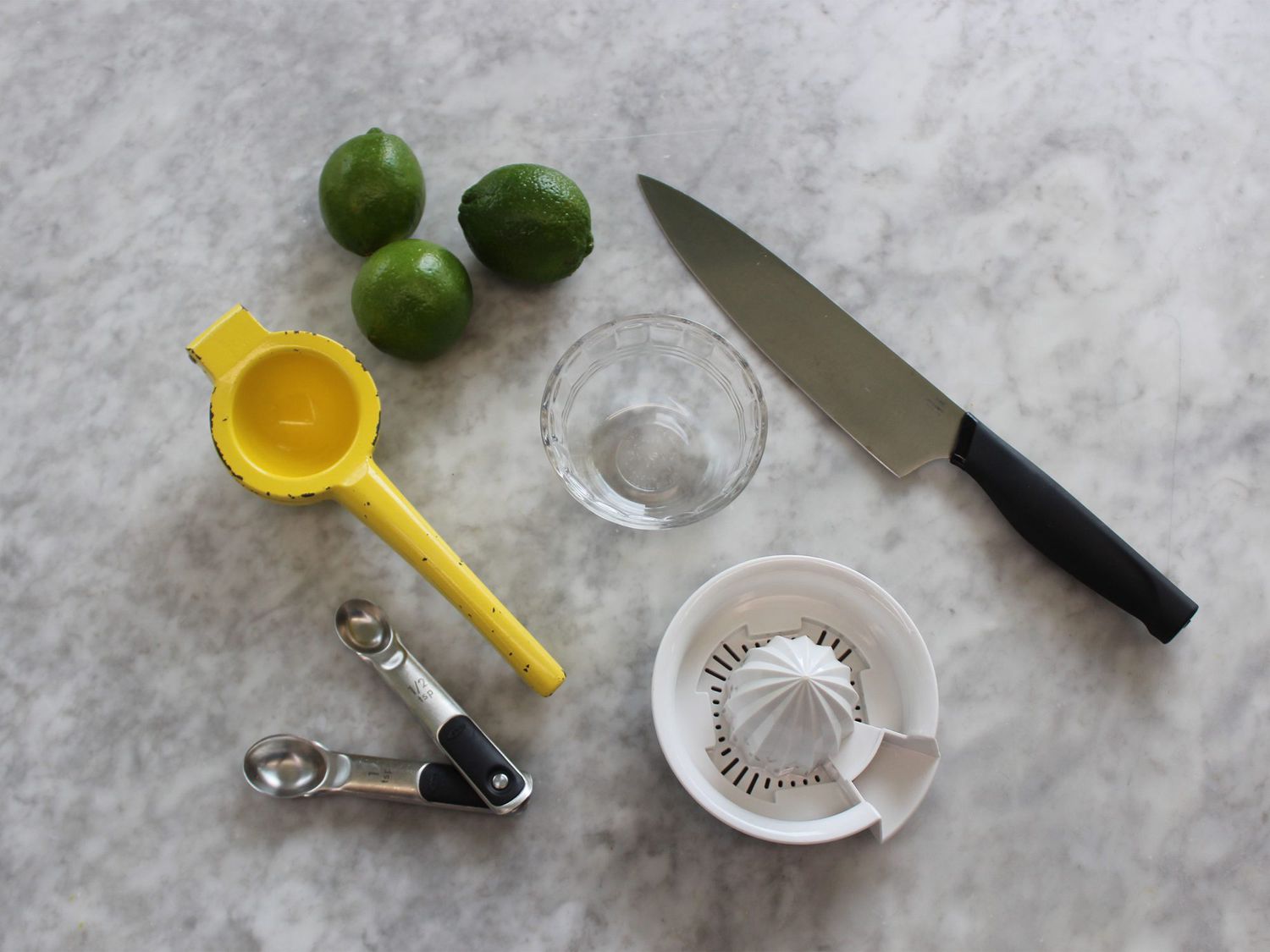 Limes, juicers, knife, bowl, and measuring spoons on countertop