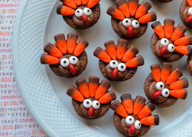 Brownies baked in mini muffin cups, decorated with candy eyes, red M&M beaks, and fall candy corn tail feathers