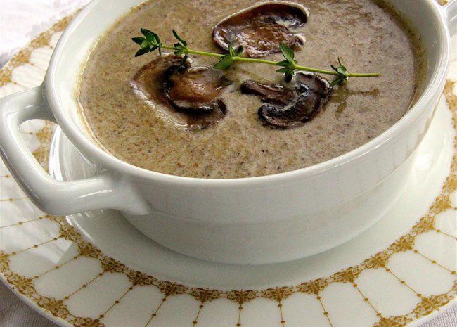 closeup of an appealing bowl of cream of mushroom soup garnished with three sauteed mushroom slices and a sprig of fresh thyme