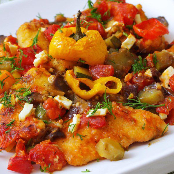 A colorful platter of chicken breasts with yellow bell pepper slices and diced tomatoes garnished with parsley