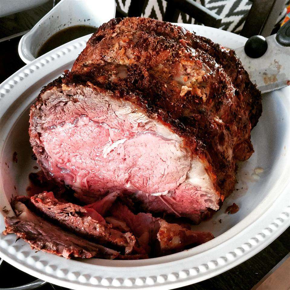 Prime rib with juicy-looking pink interior on a white ceramic serving dish