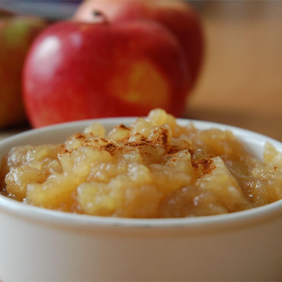 a white bowl with cinnamon-dusted applesauce, with red apples in the background