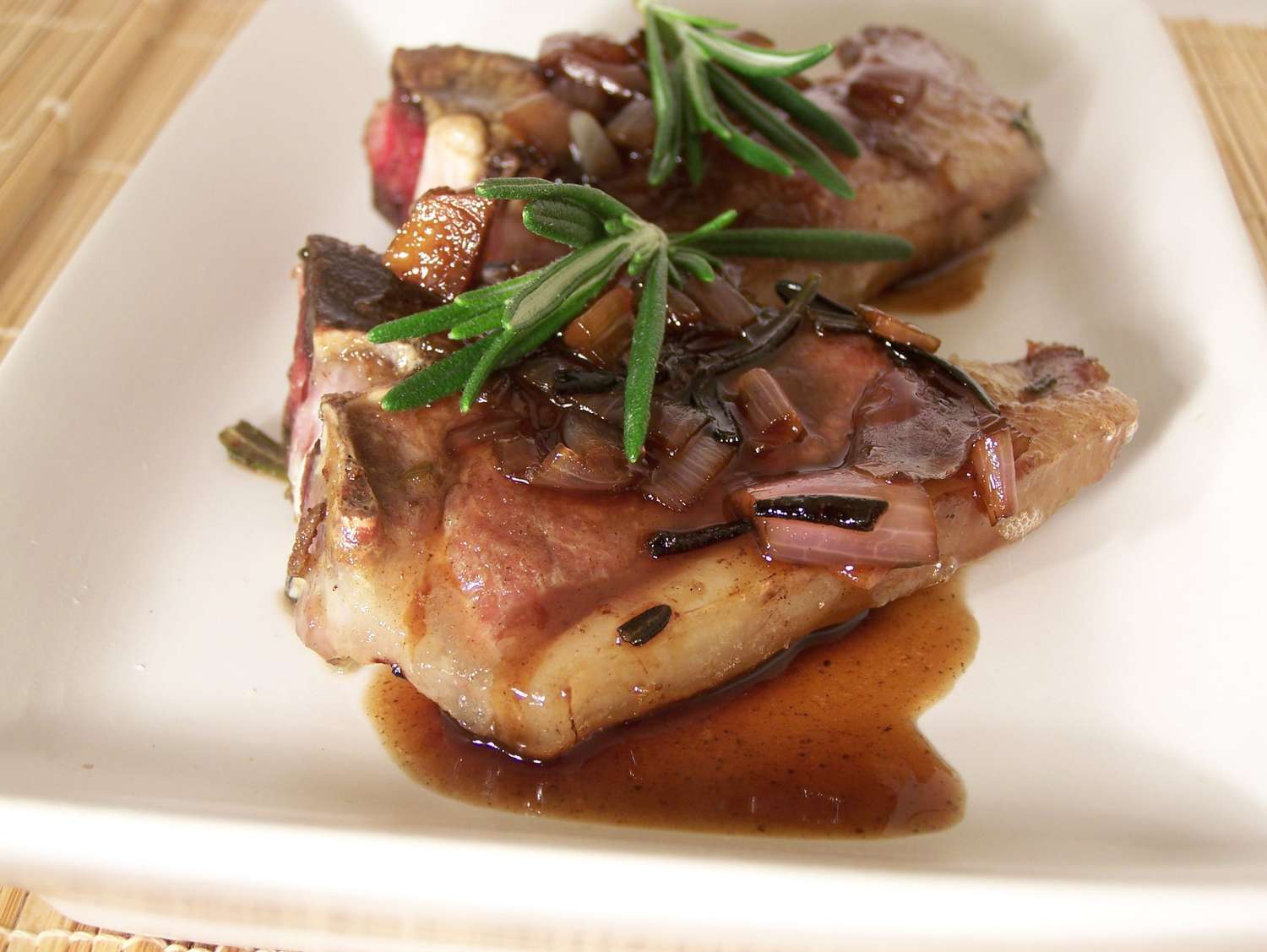 two Lamb Chops with Balsamic Reduction garnished with fresh rosemary on a plate