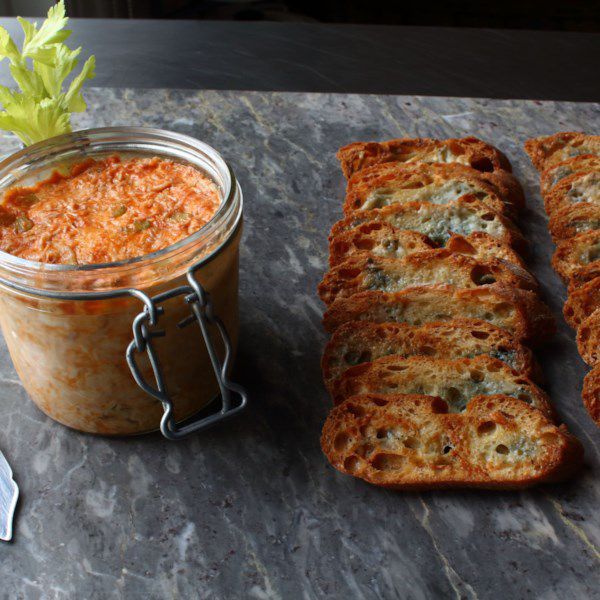 a small mason jar with Buffalo chicken dip, with crostini on the side for dipping