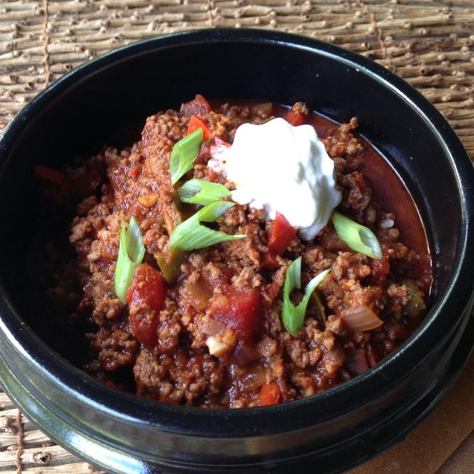a bowl of chili without beans, topped with a dollop of sour cream and sliced green onions