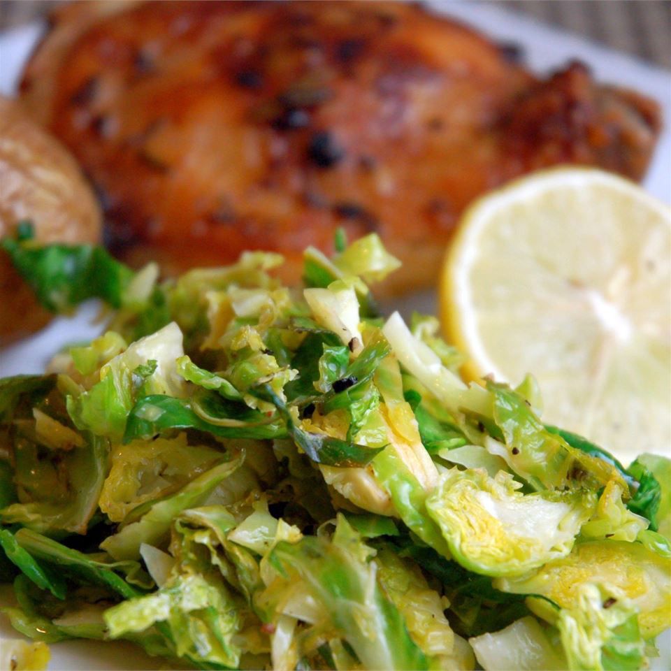 closeup of a serving of shredded Brussels sprouts garnished with a lemon slice with roast chicken in the background