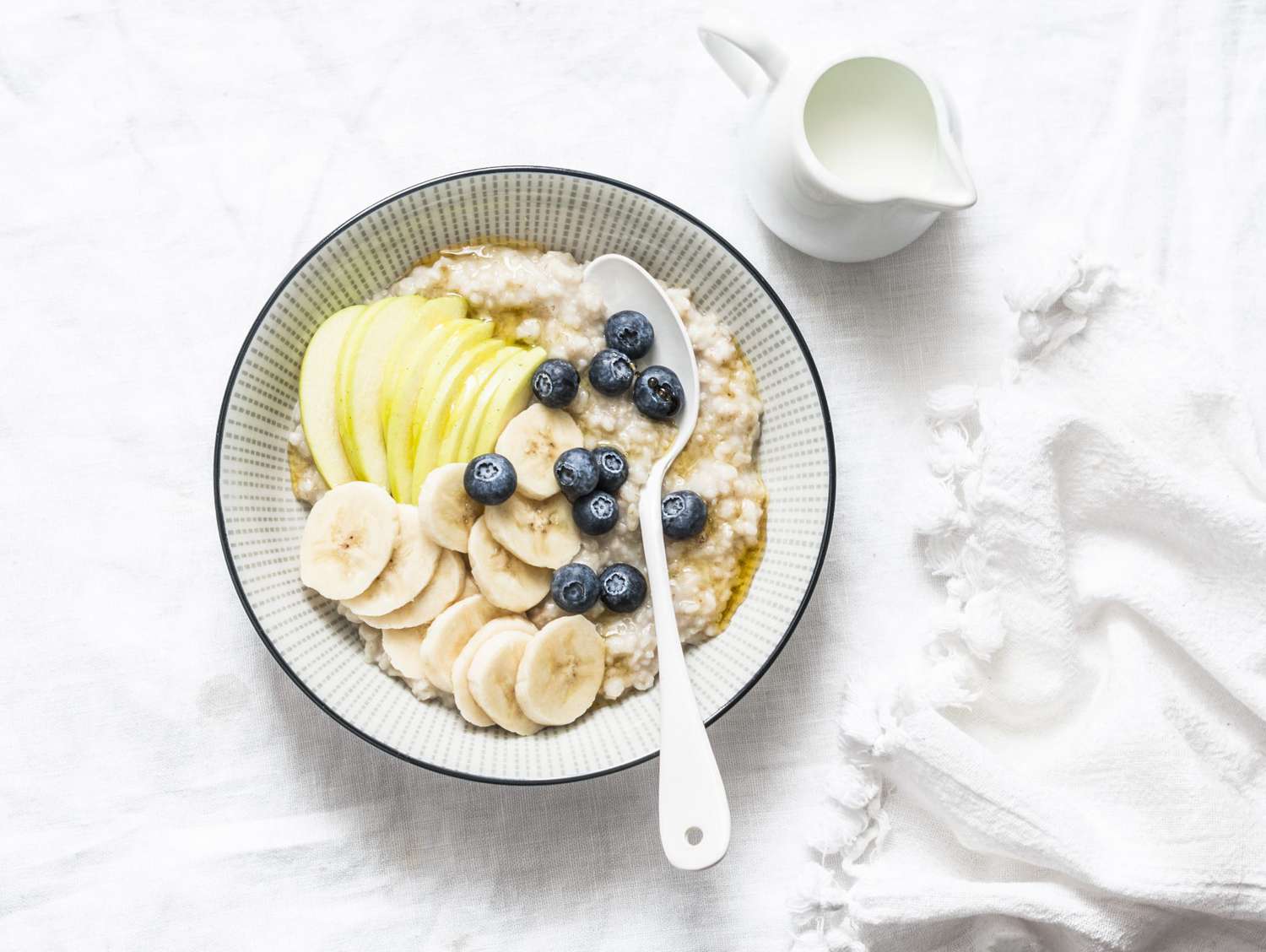 Oats breakfast coconut milk porridge with apple, banana, blueberry and honey on a light background, top view. Vegetarian healthy food