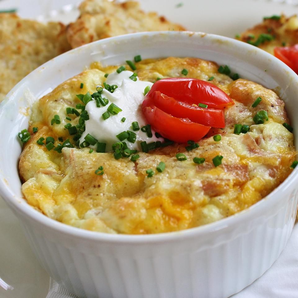 a small casserole dish contains baked eggs with sour cream, chives, and sliced tomatoes on top