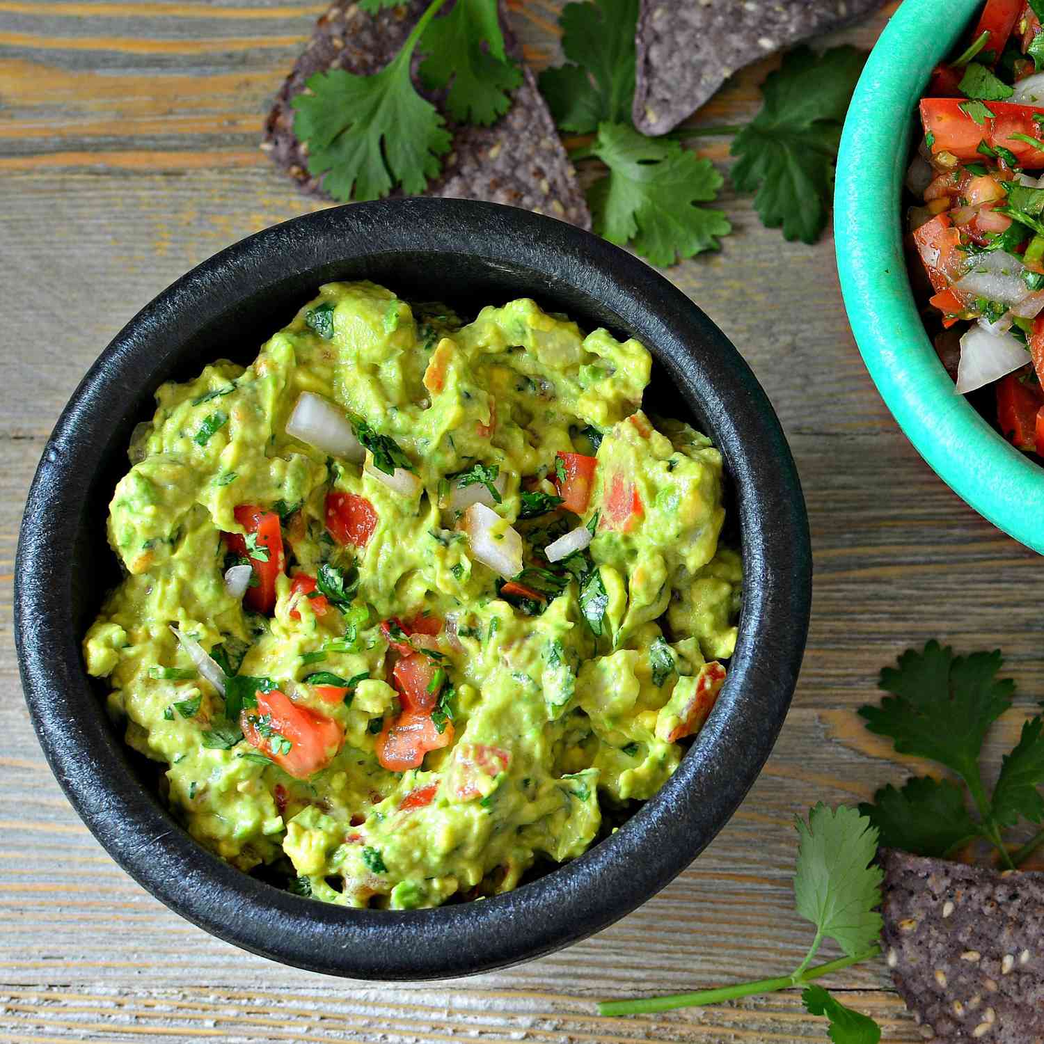 a black bowl is filled with green guacamole with bits of tomato and red onion peeking through