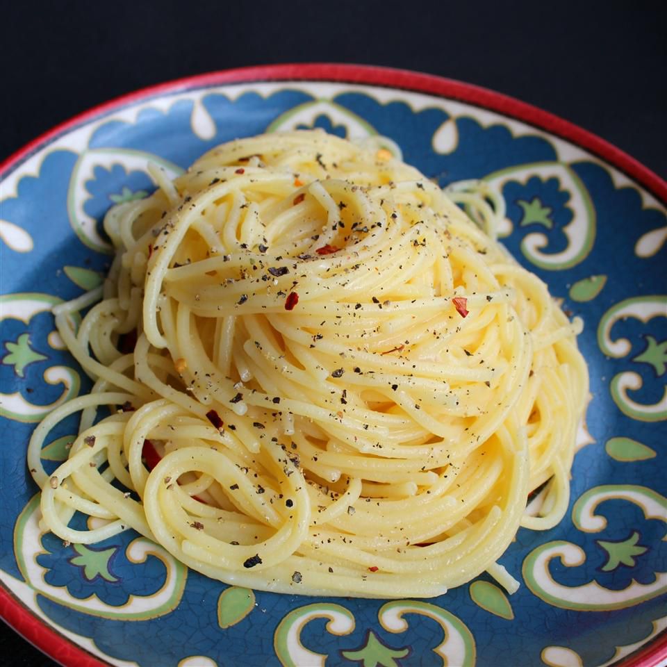 a coiled mound of peppery spaghetti on a ceramic plate with a blue and white design, with a red rim