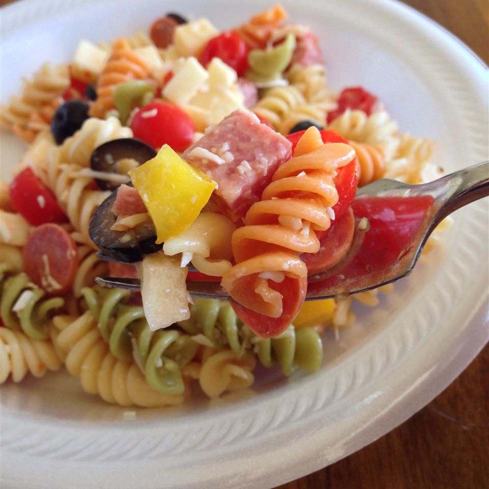 A tricolor fusilli pasta salad with sliced black olives and chopped salami on a white plate