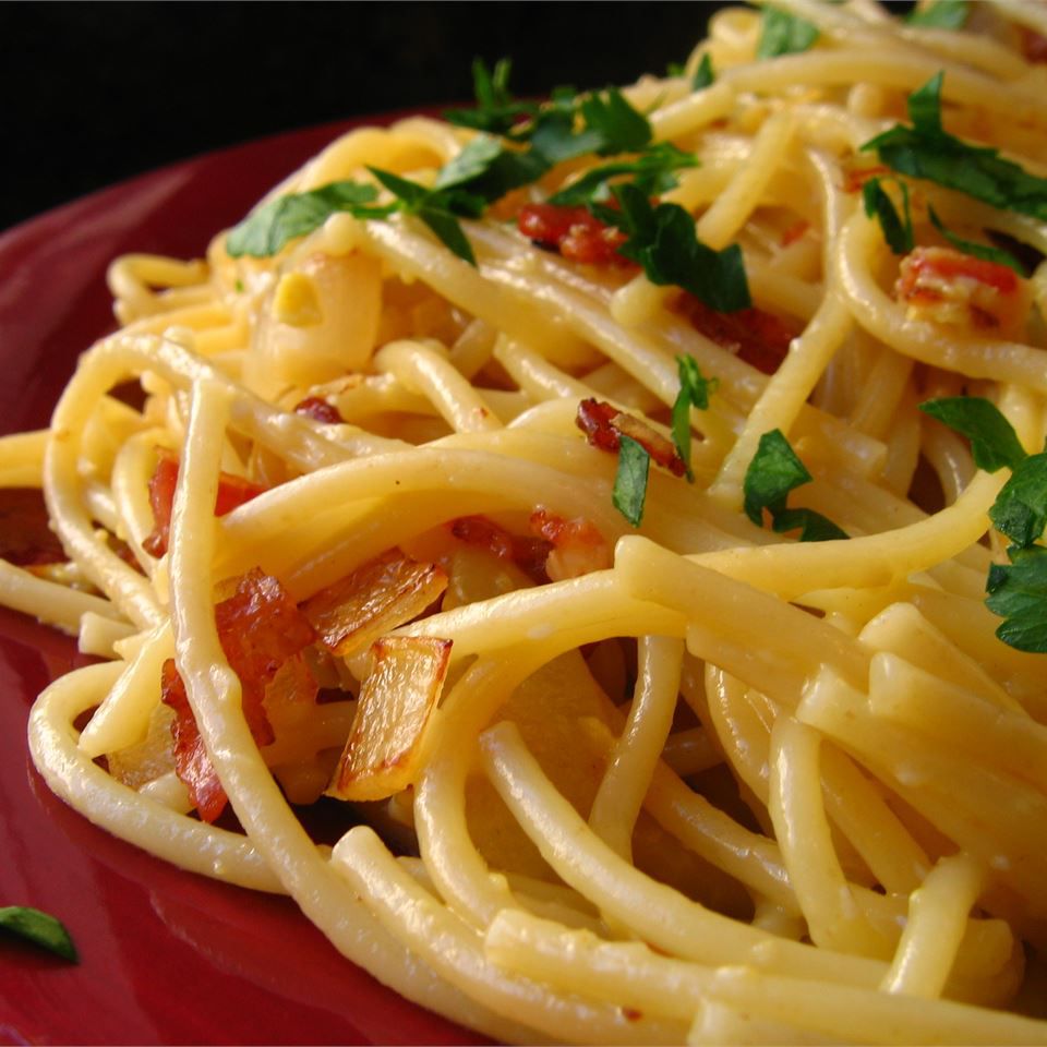 closeup of creamy-looking spaghetti with bacon, garnished with parsley and served on a red plate