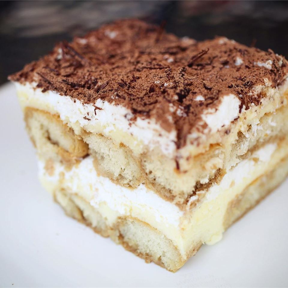 side view of a square slice of tiramisu showing the layers of ladyfingers and custard, topped with chocolate shavings