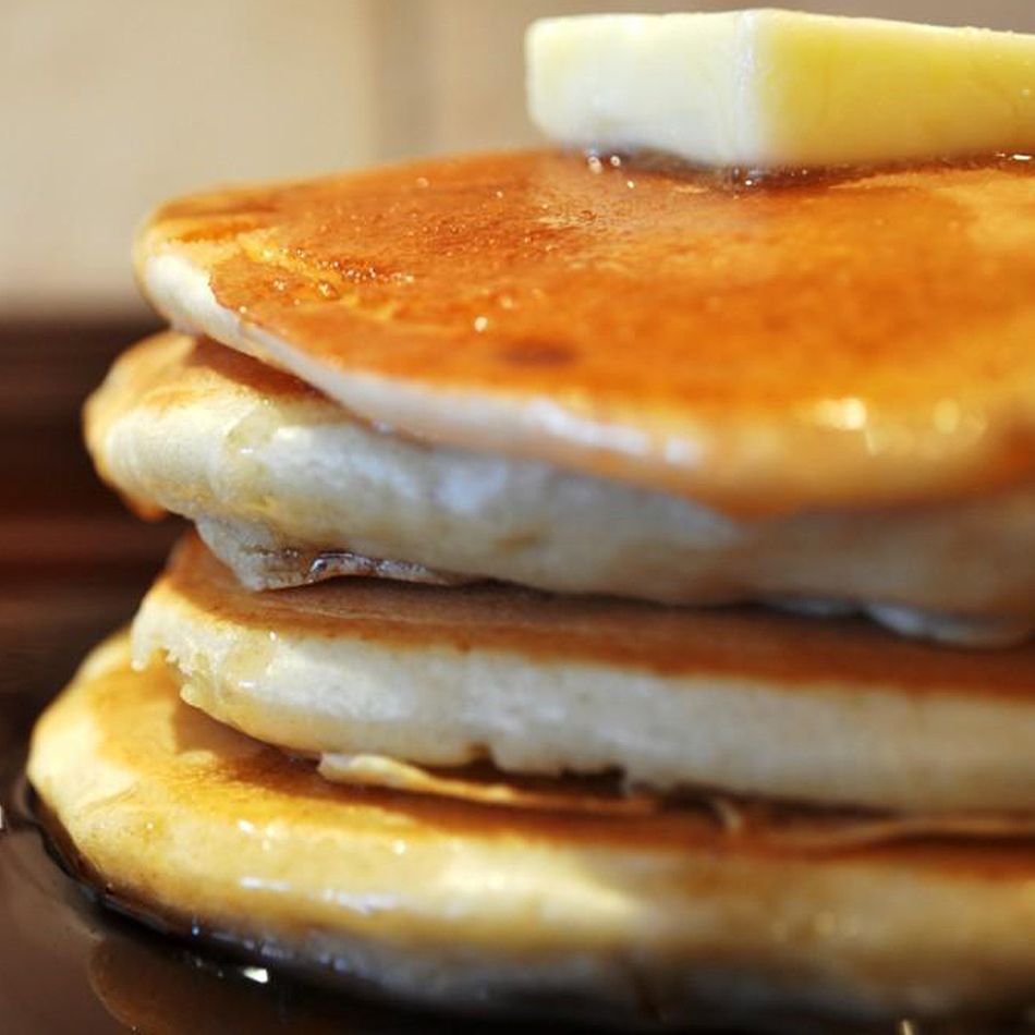 A stack of pancakes topped with a pat of butter, dripping with maple syrup
