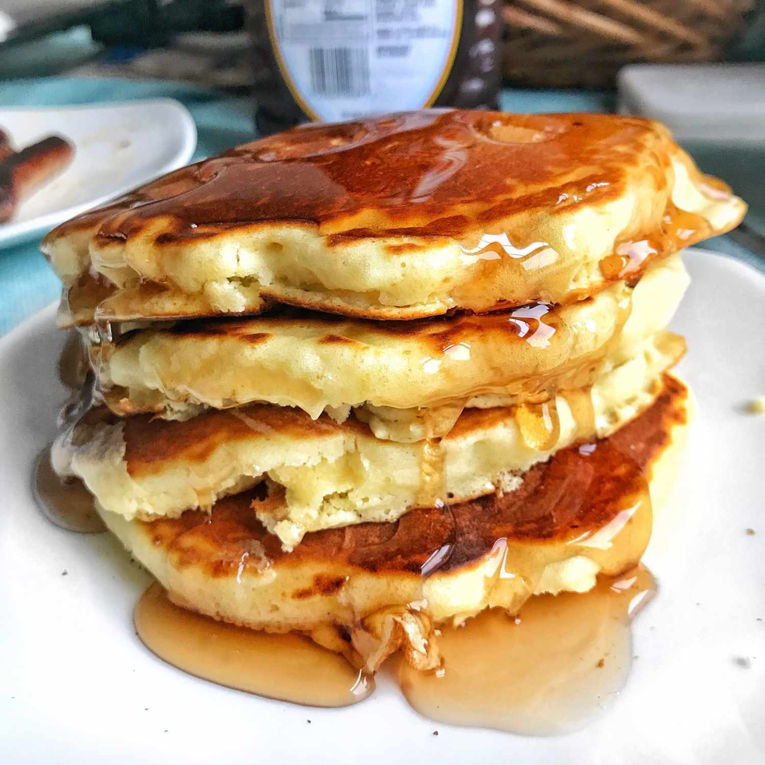 side view of a stack of four pancakes on a plate with syrup