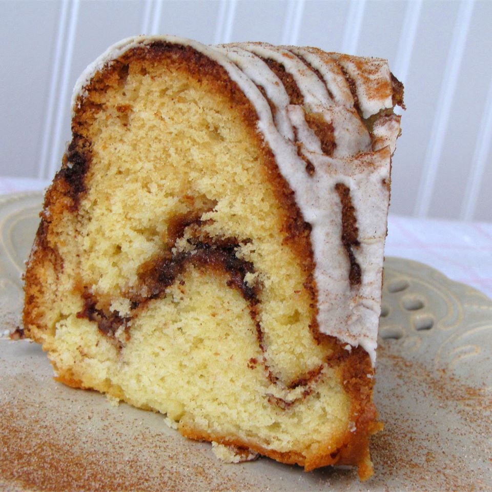 a slice of cake with a white icing drizzle and a ribbon of cinnamon streusel on a white plate