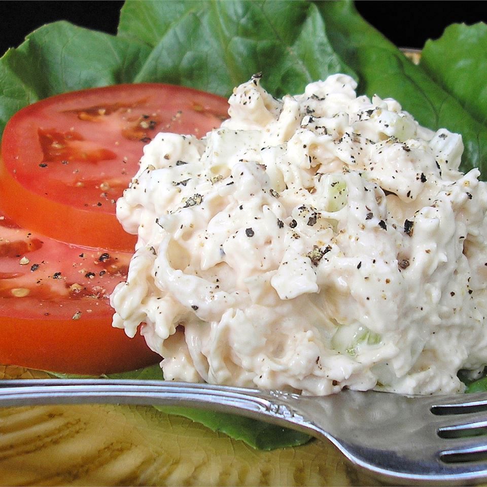 a scoop of chicken salad topped with fresh ground pepper on a plate with sliced tomatoes and lettuce leaves