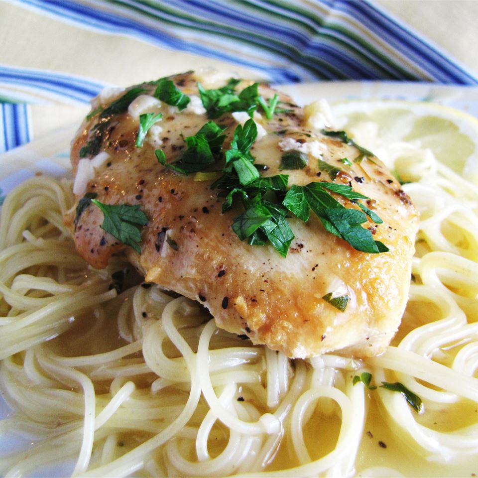 a chicken breast served on a bed of spaghetti, garnished with chopped parsley