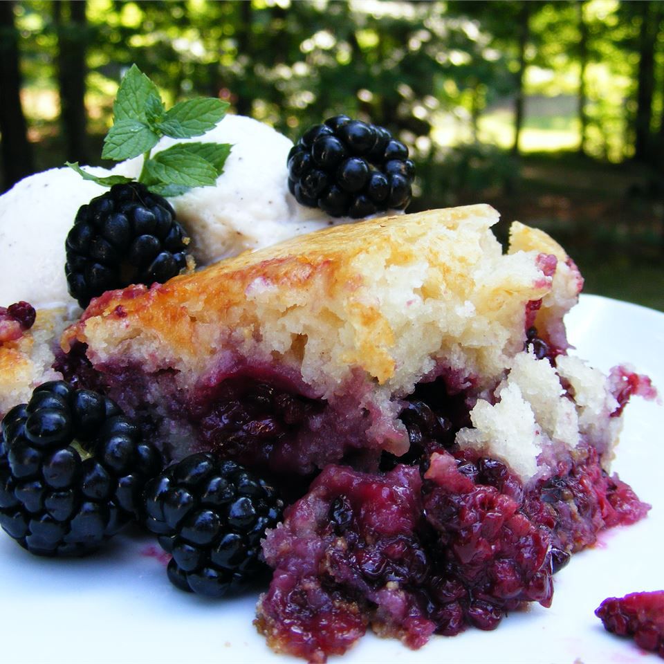 a serving of blackberry cobbler garnished with raw blackberries, a mint sprig, and a scoop of vanilla ice cream