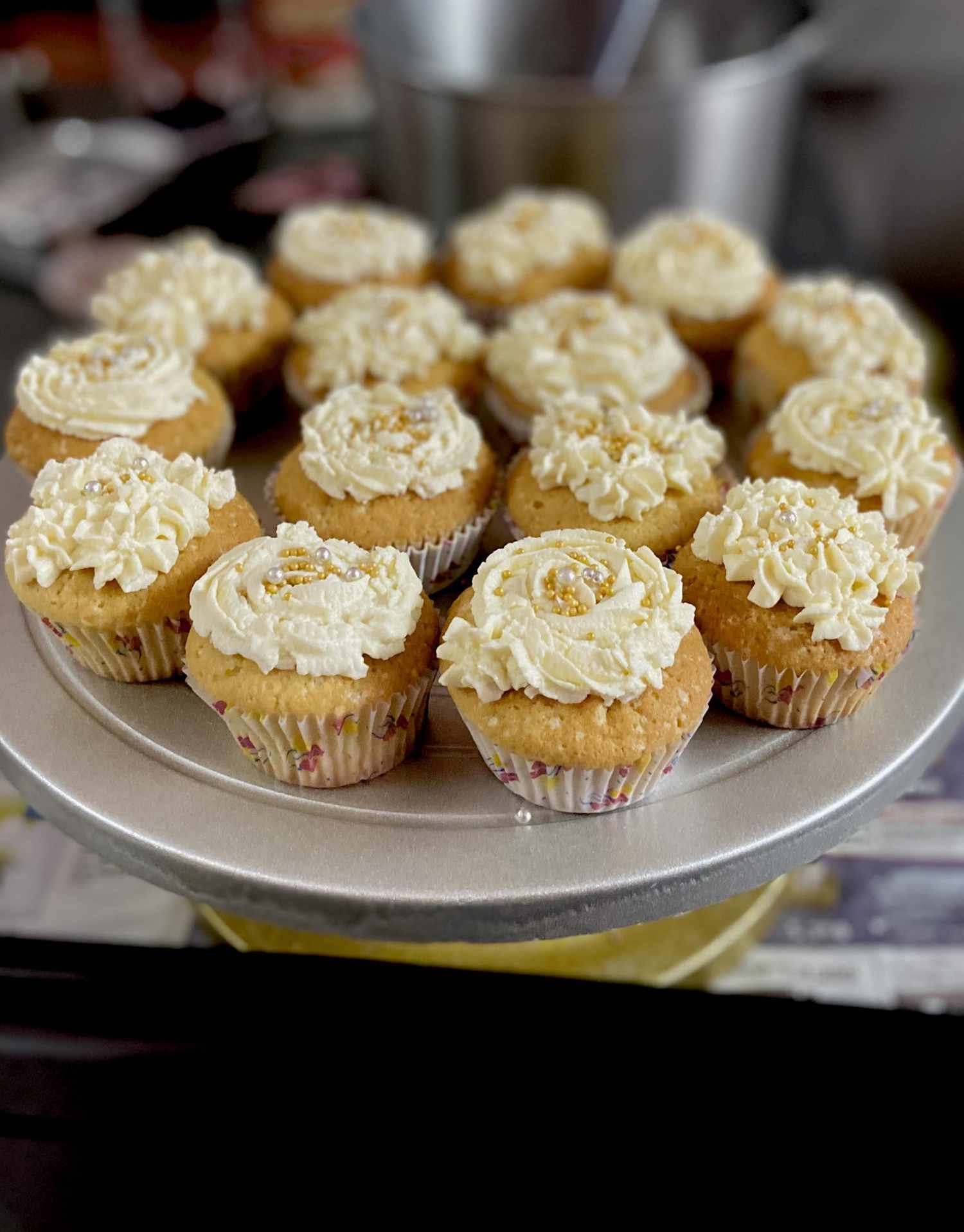 a plate holding 15 cupcakes with piped white frosting and gold sprinkles