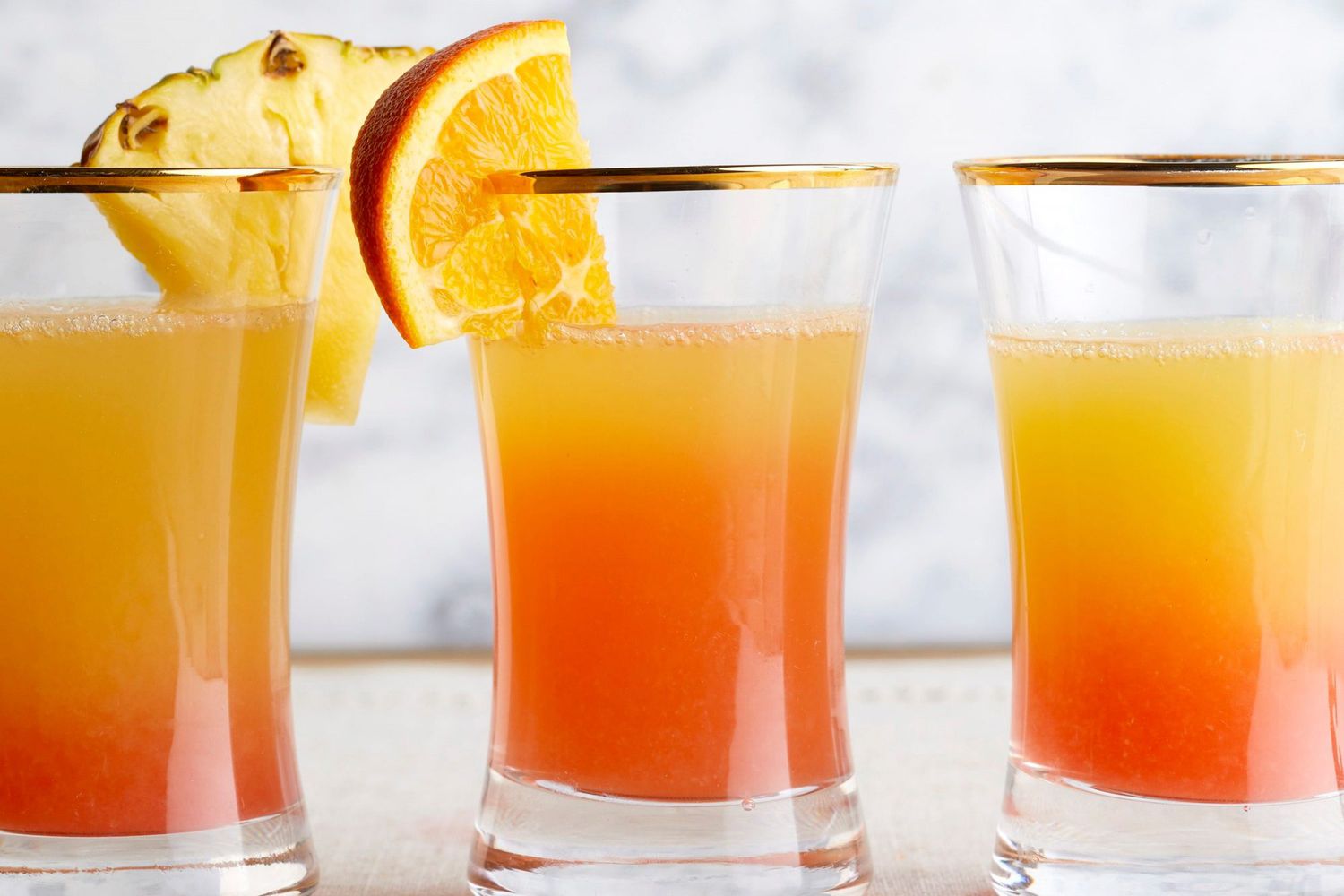 mimosas with orange and pineapple garnishes in short glasses