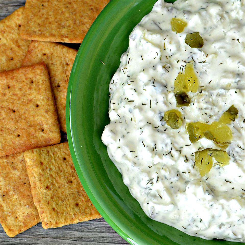 top-down view of a creamy-looking dip garnished with chopped pickles with crackers on the side