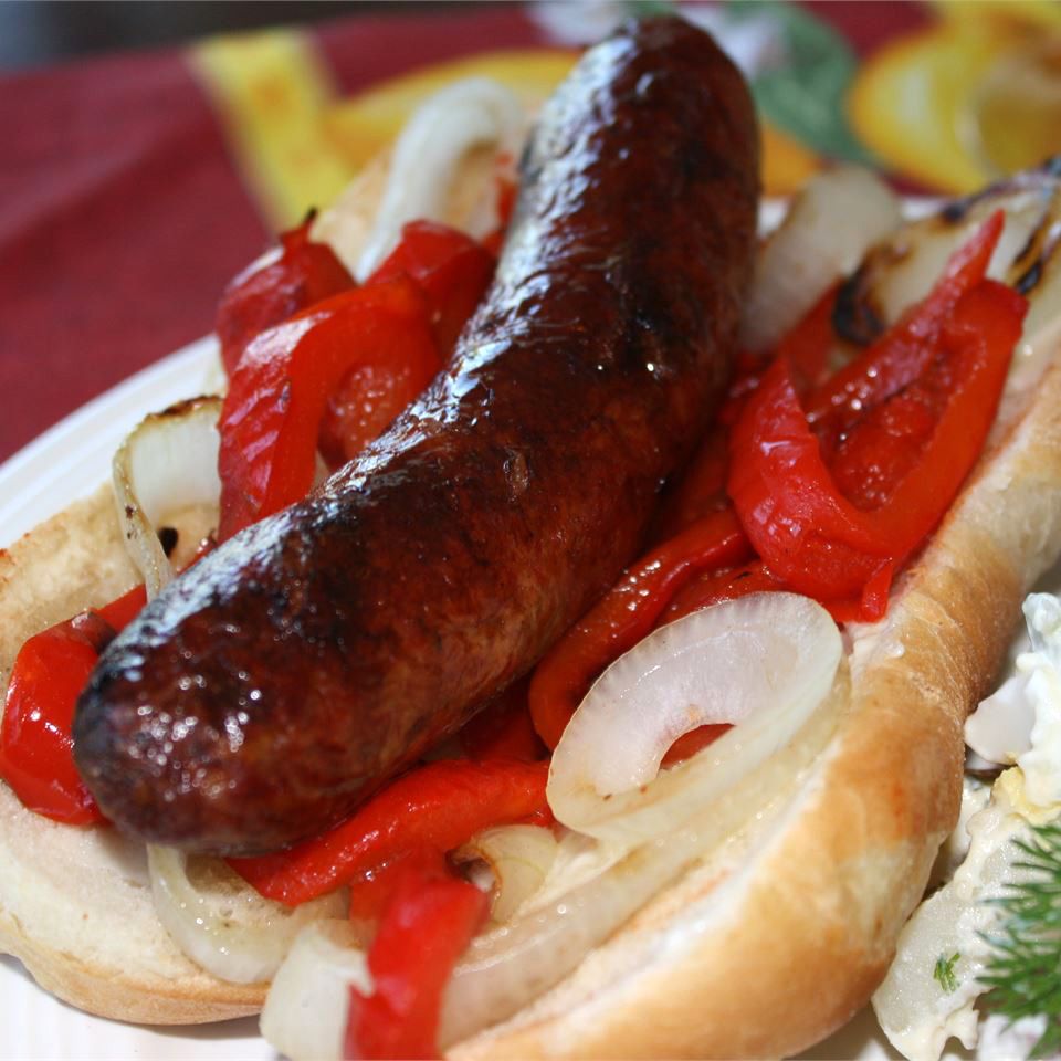 a grilled sausage on a bun with onions and red bell peppers