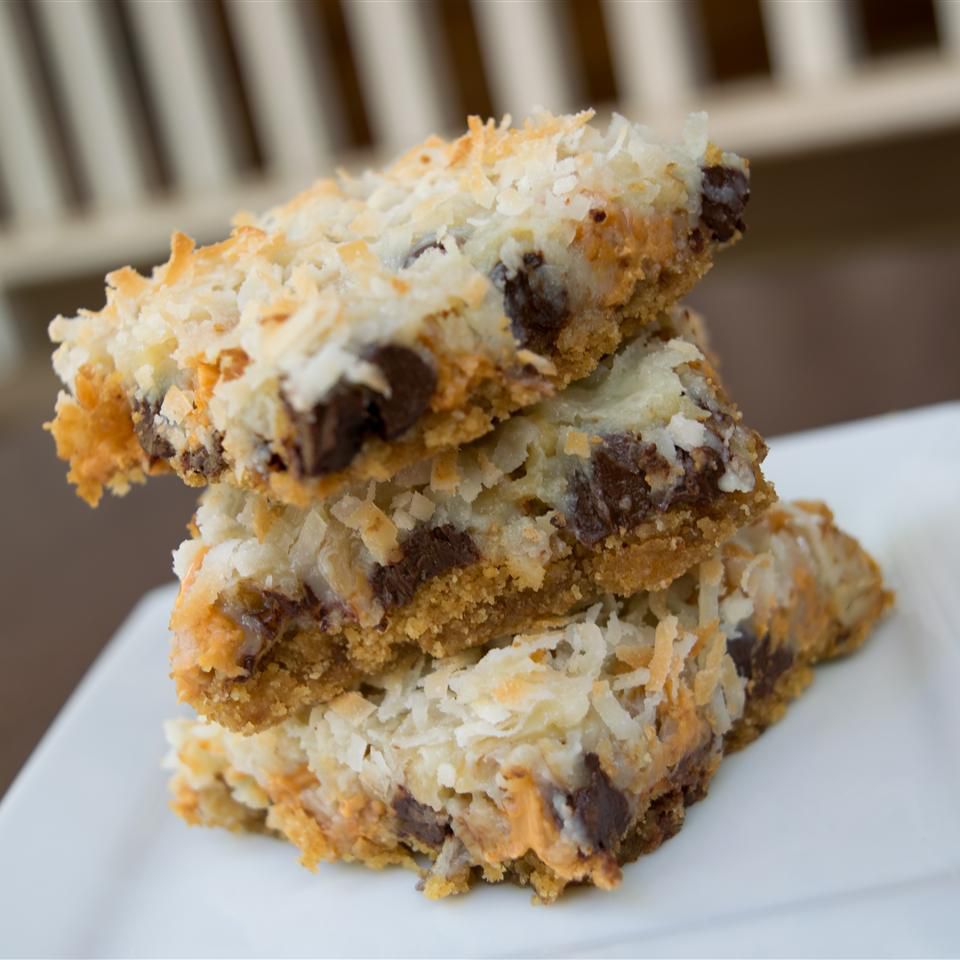 a stack of three coconut-topped 7 layer bars on a square white plate