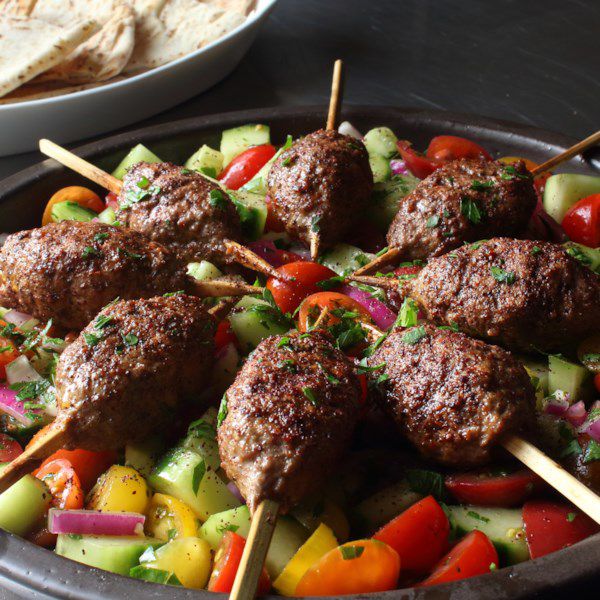 ground beef kabobs on wooden skewers over a bed of vegetables