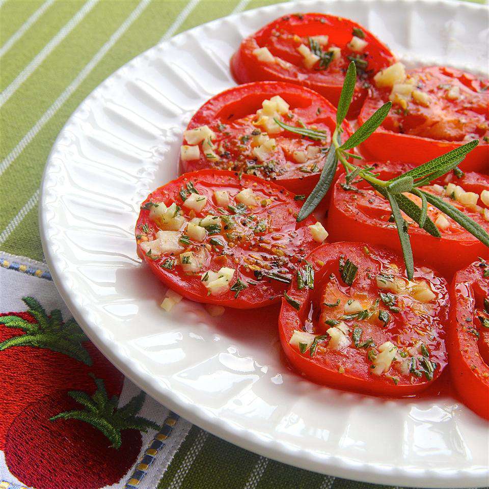 Ripe red tomato slices topped with minced garlic and a sprig of fresh rosemary