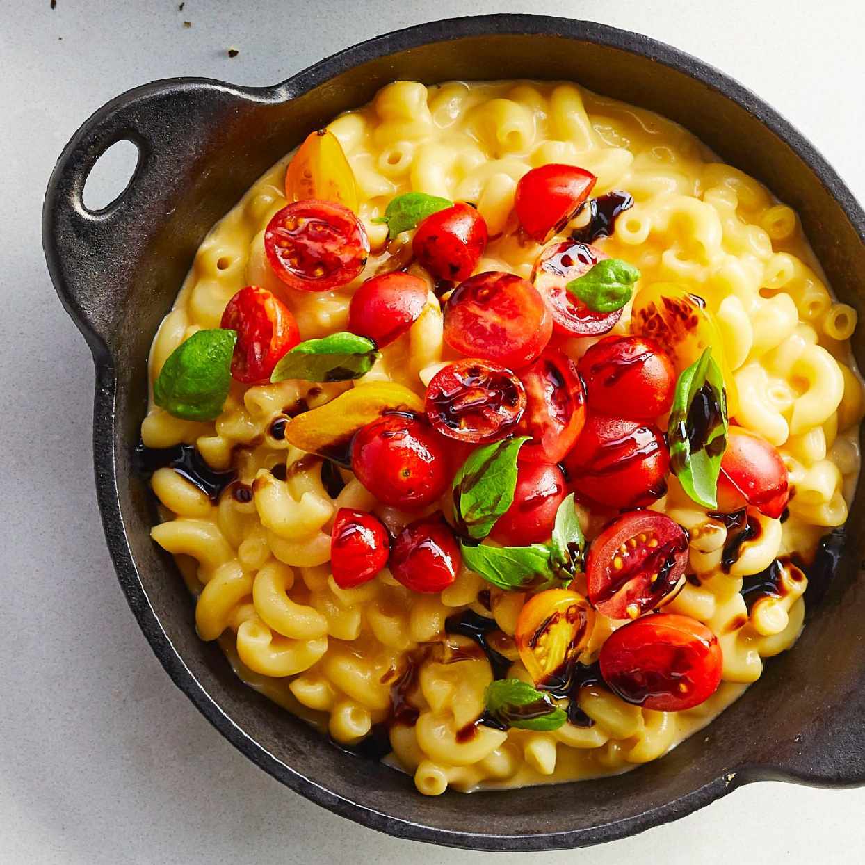 Bowl of mac and cheese with cherry tomatoes, basil leaves, and balsamic glaze over the top