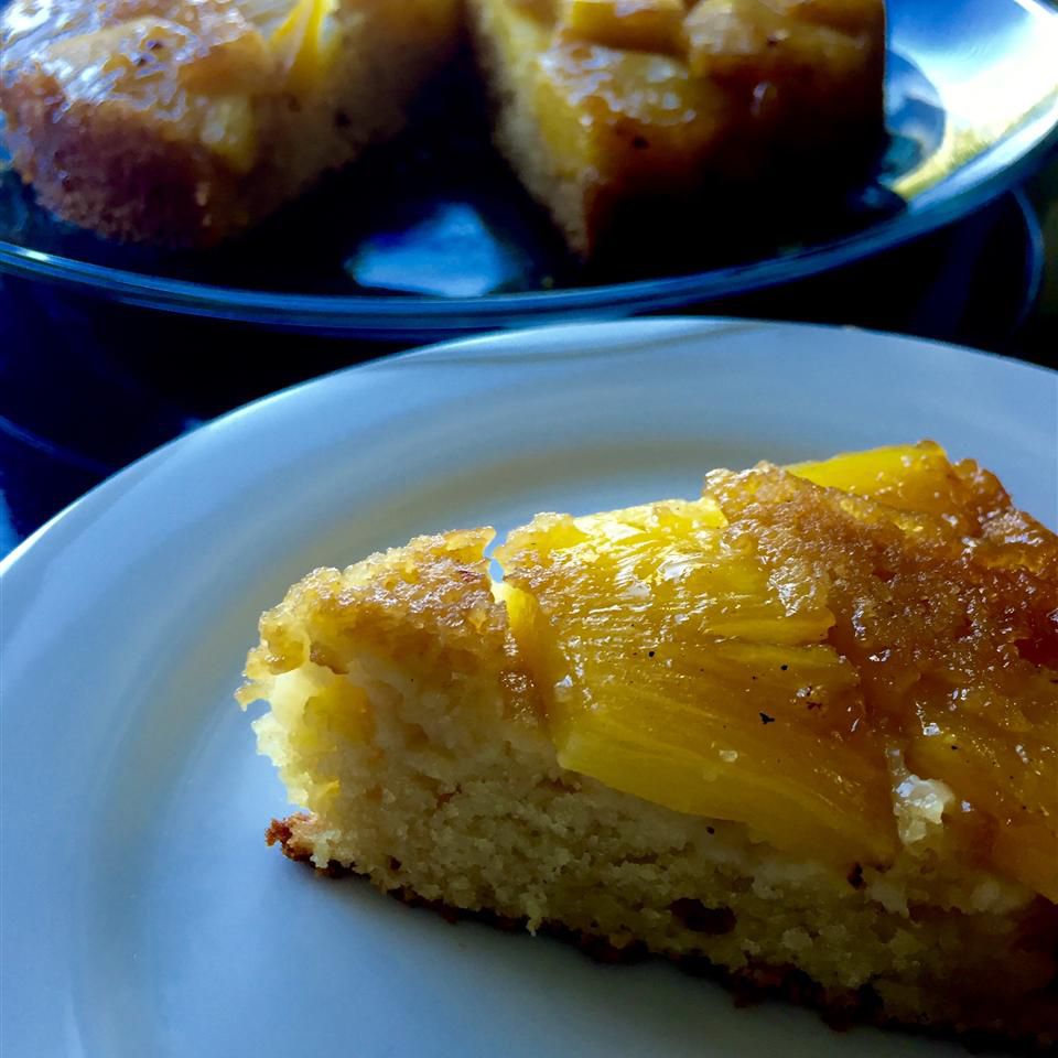 A slice of cake topped with pineapple pieces in the foreground, with the rest of the cake in back
