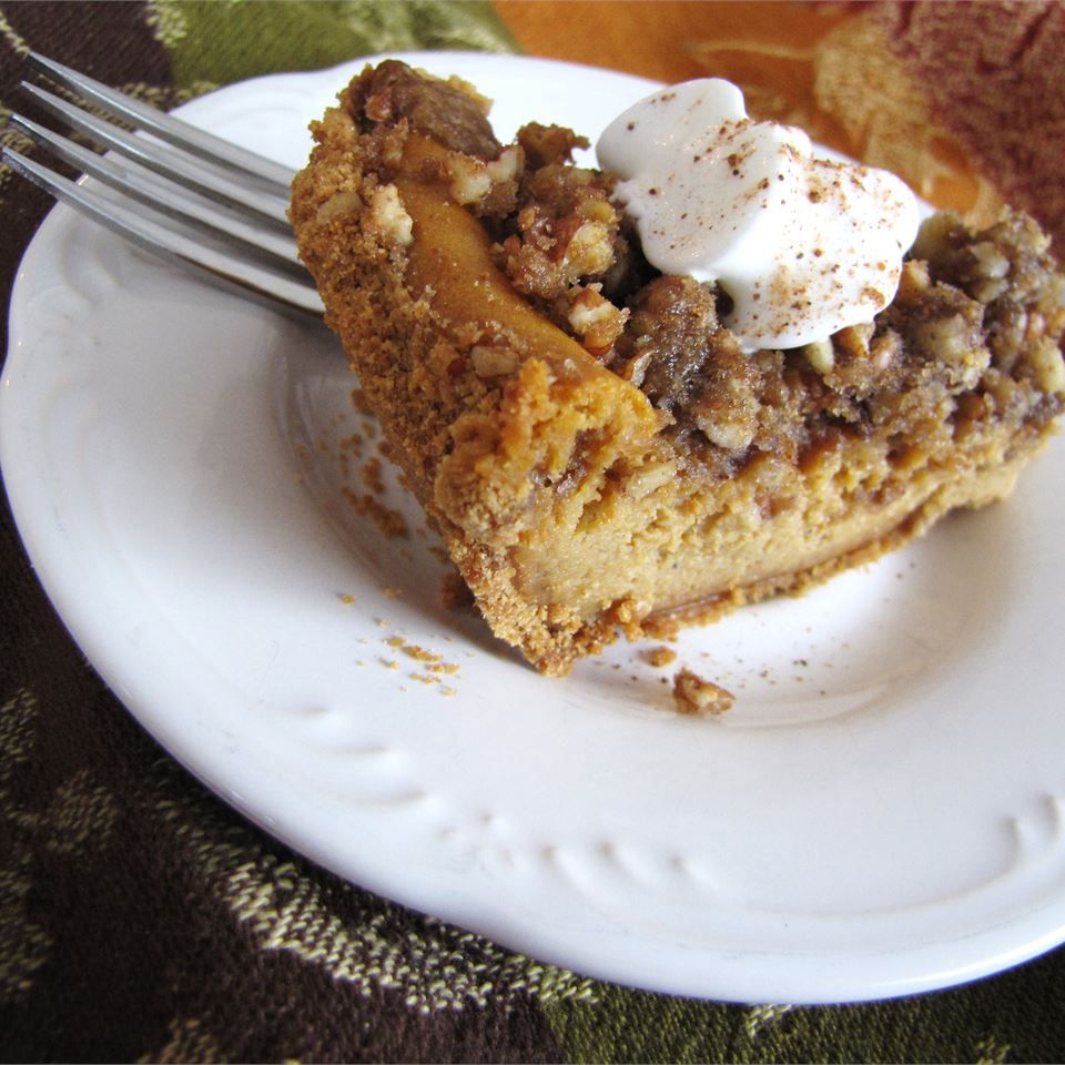 A slice of pecan-topped cheesecake on a white plate, garnished with cinnamon-dusted whipped cream