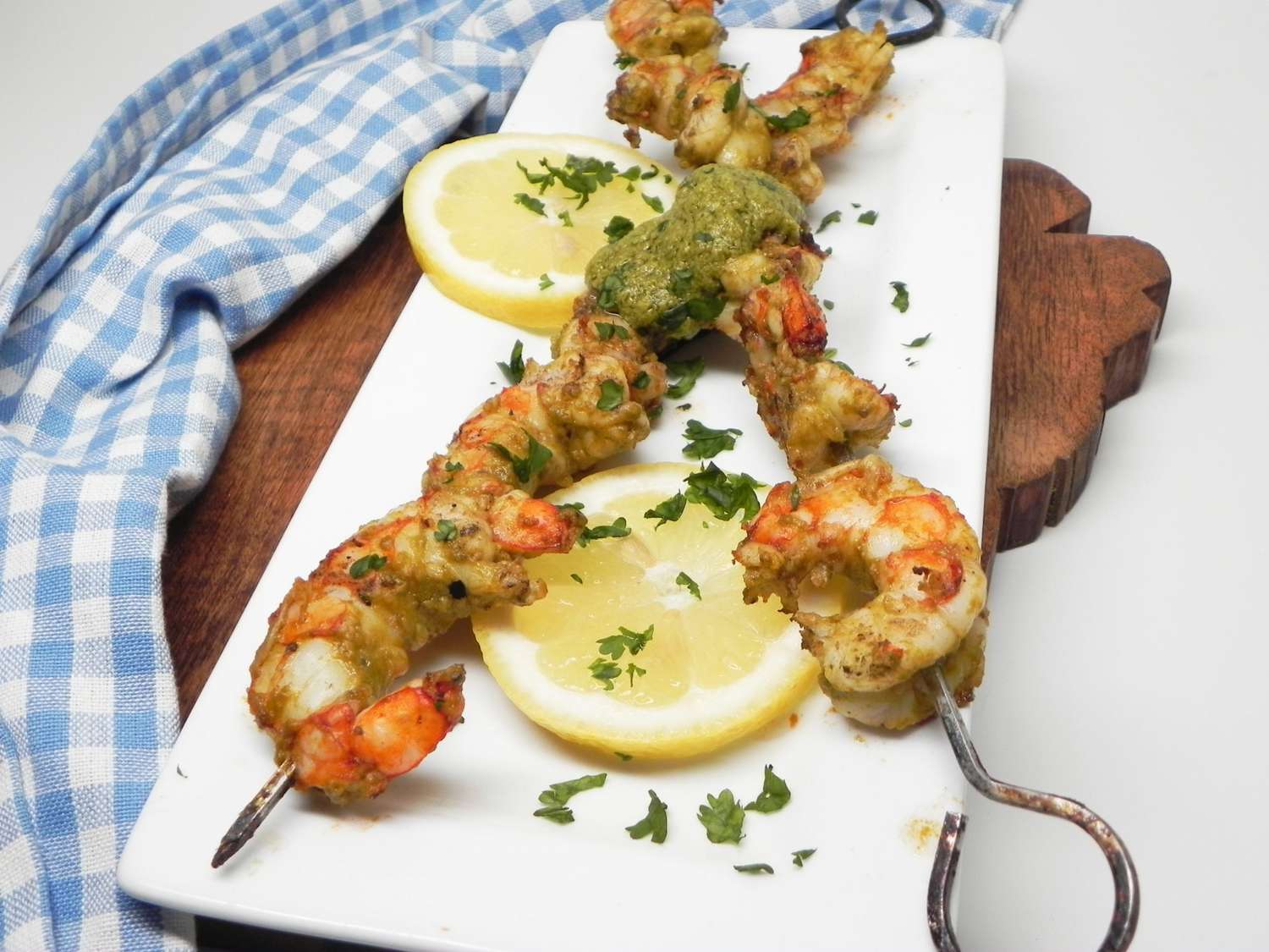 Two skewers of shrimp on a white platter with lemon slices and parsley